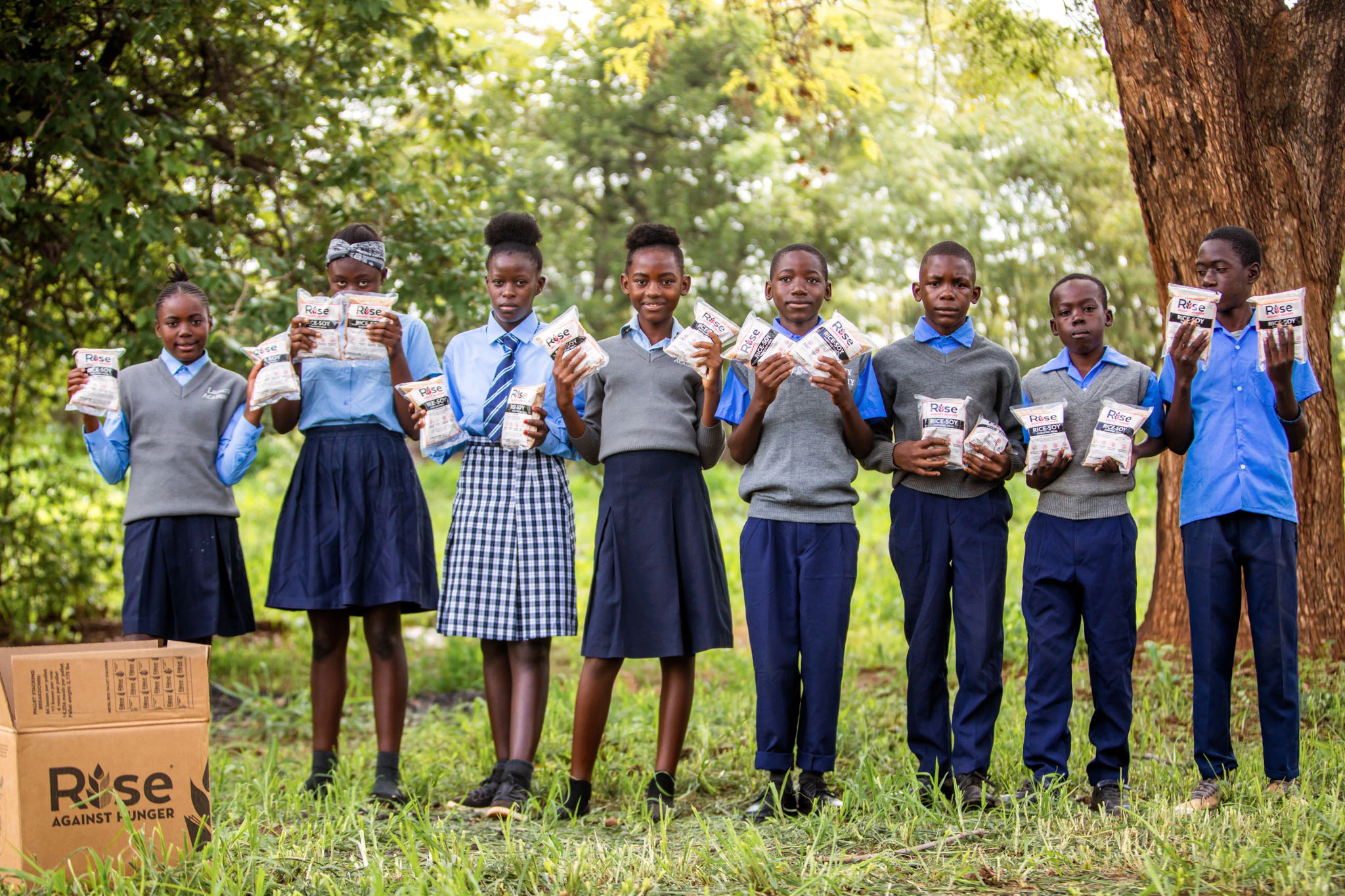 Students in Zambia stand in a line smiling holding Rise Against Hunger Meal Bags