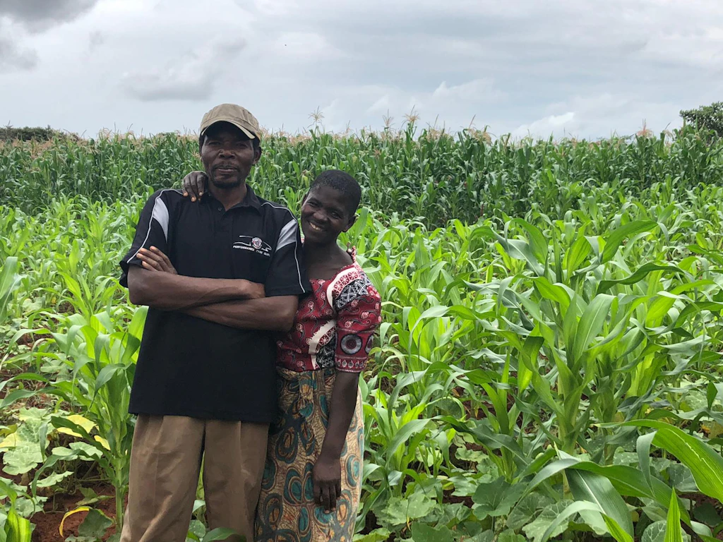male and female farmer smile in foreground of their crops